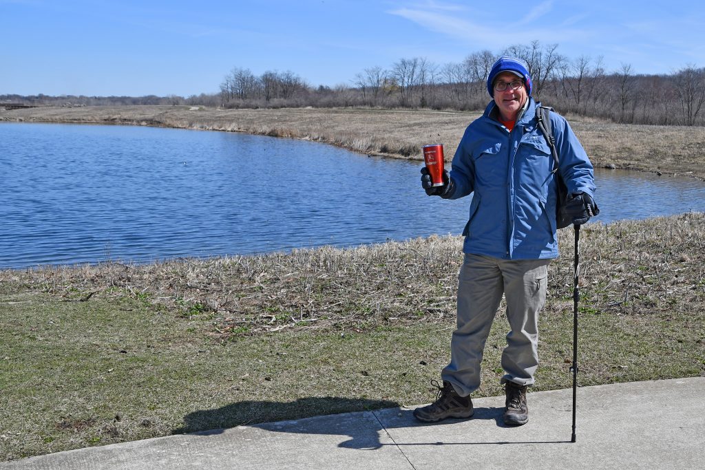 Bolingbrook resident Mike Slowik, 62, was the first person to finish the Forest Preserve District of Will County’s Spring Ninety-fiver Challenge, which began March 1 and runs through June 30. Slowik is pictured in full hiking gear – including his essential coffee mug – at Whalon Lake preserve in Naperville. –Photo by Forest Preserve staff Glenn P. Knoblock.